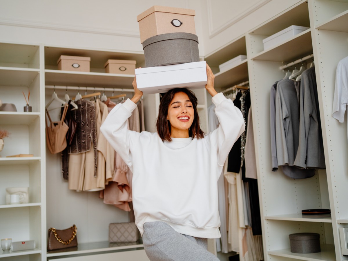 Frau, die beim Kleiderschrank ausmisten mehrere Kartons auf dem Kopf trägt.