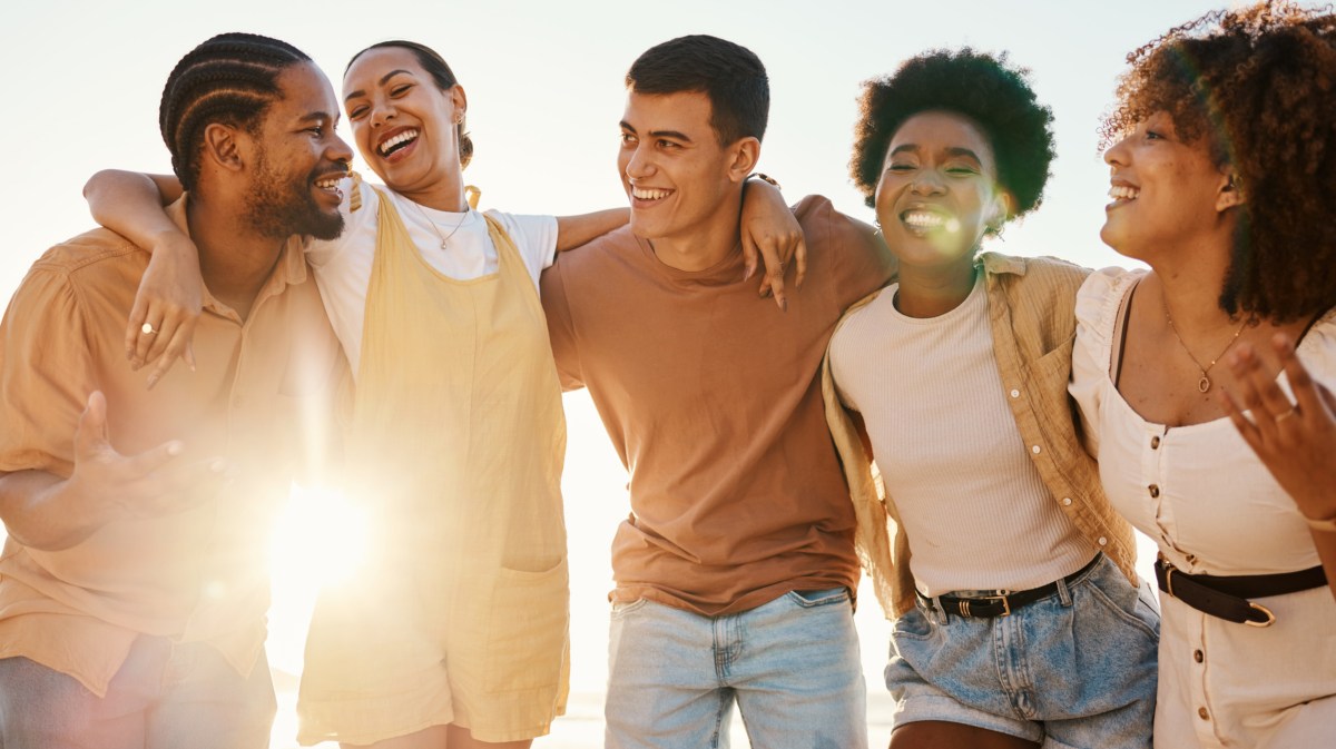 Freunde, die sich zusammen umarmen und lachen, während Sonnenstrahlen durch sie durch scheint