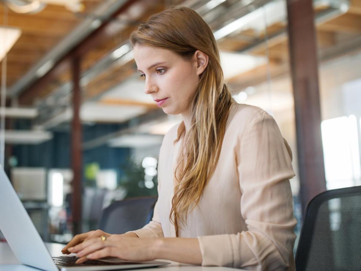 Frau mit langen Haaren sitzt am Schreibtisch am Laptop.