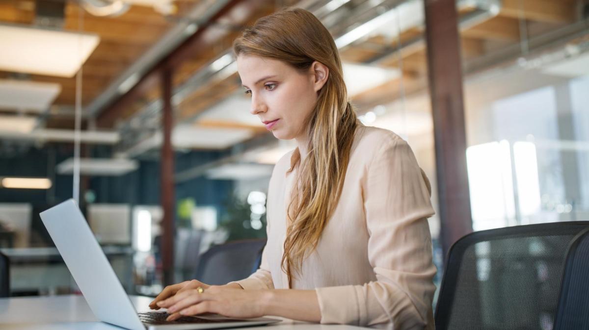 Frau mit langen Haaren sitzt am Schreibtisch am Laptop.