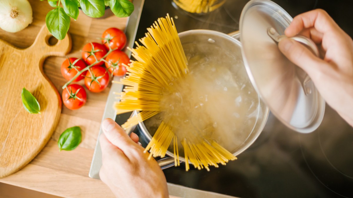 Person kocht Spagetti und öffnet den Topfdeckel. Es tritt Dampf aus.