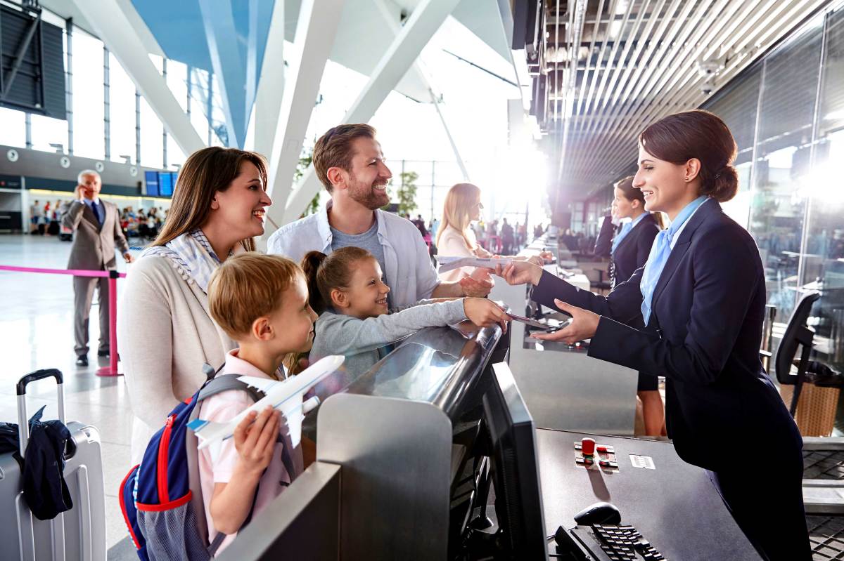 Vierköpfige Familie steht am Check-in-Schalter eines Flughafens und reicht der Mitarbeiterin die Reisepässe.