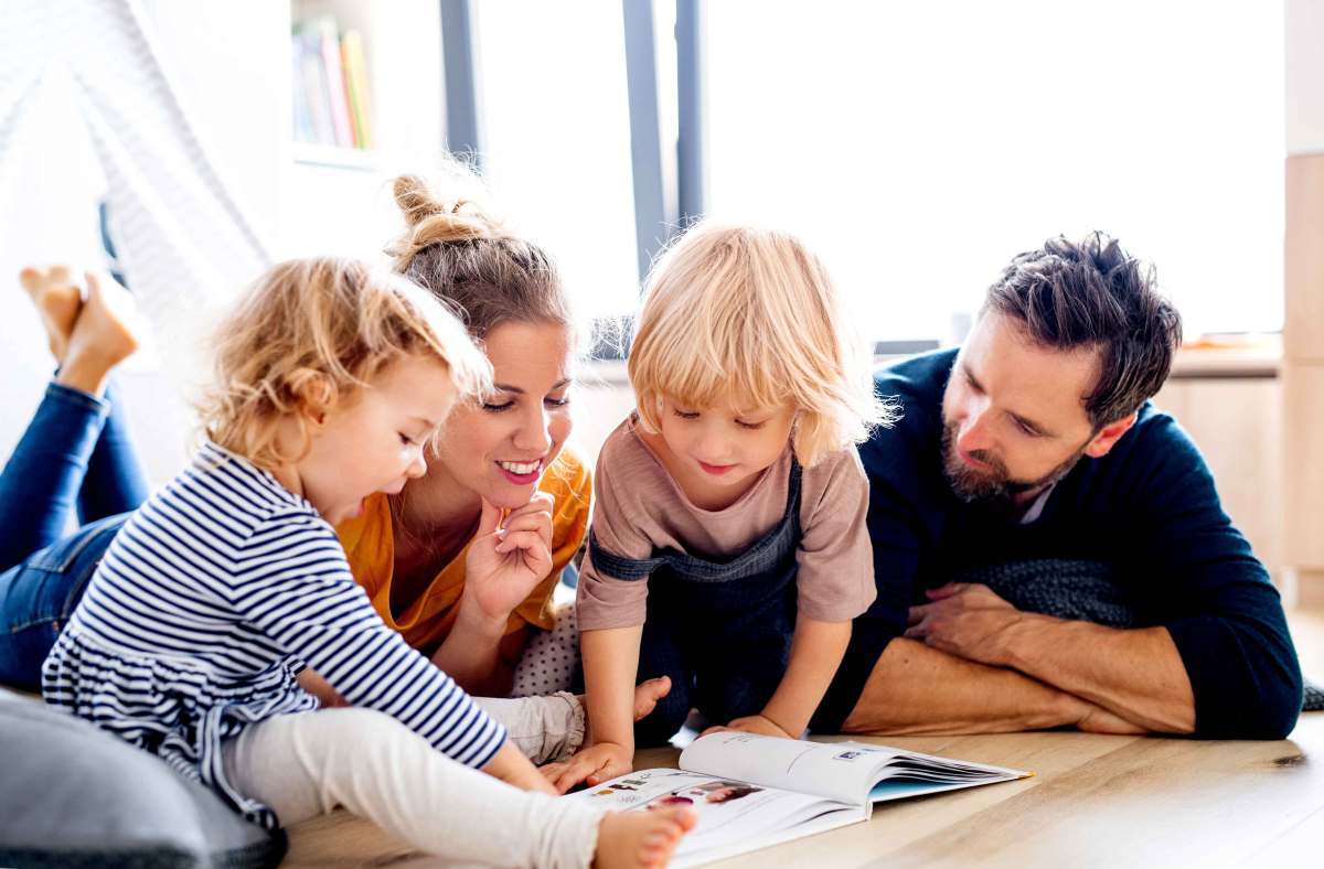 Mutter, Vater und zwei Kinder liegen auf dem Fußboden und blättern gemeinsam in einem Buch.