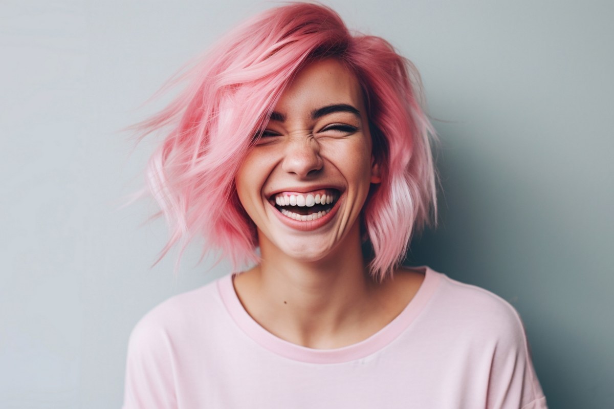 Frau mit rosa Haaren lacht vor Freude in die Kamera.