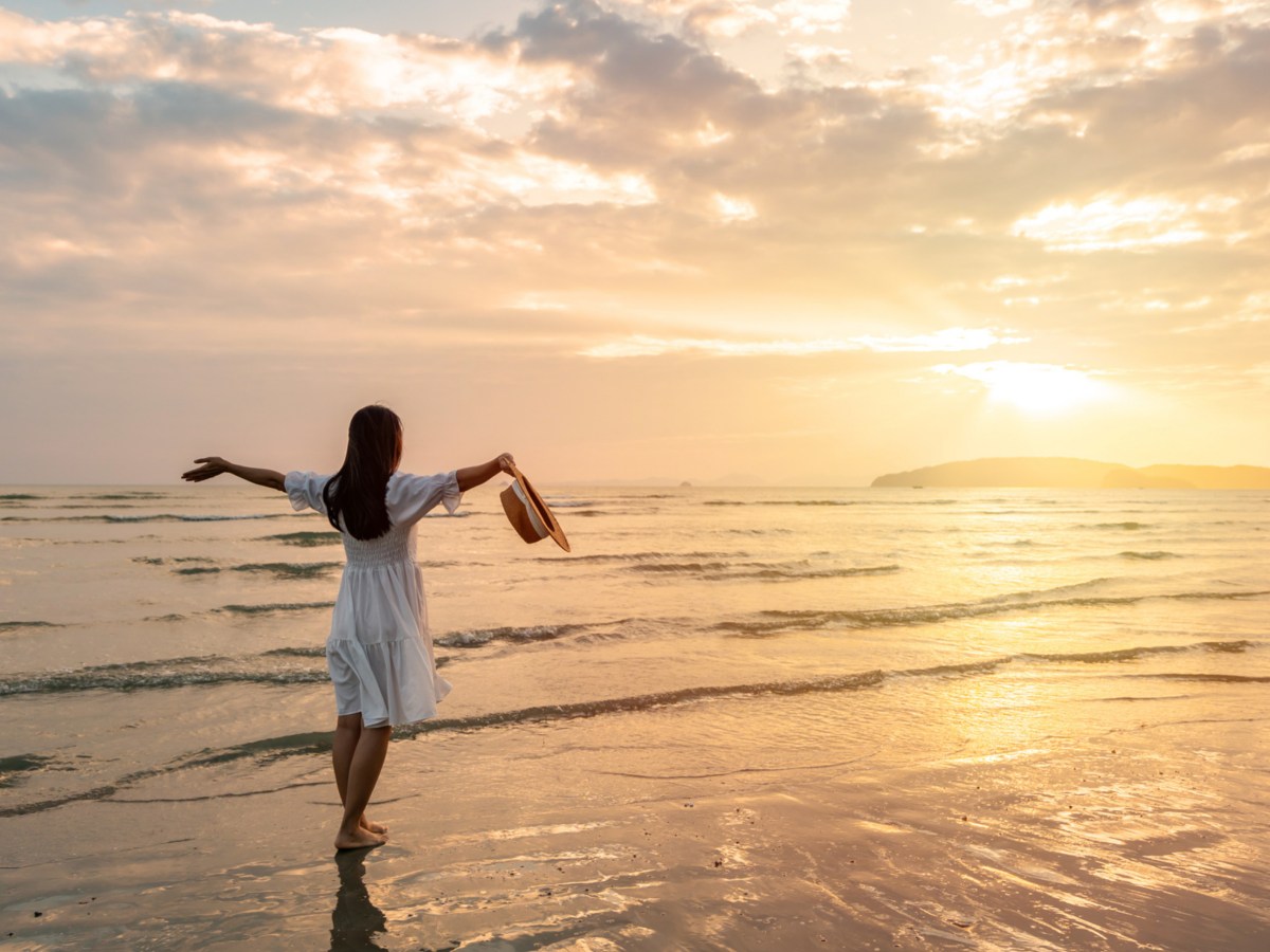 Frau im Sommerkleid am Strand bei Sonnenuntergang