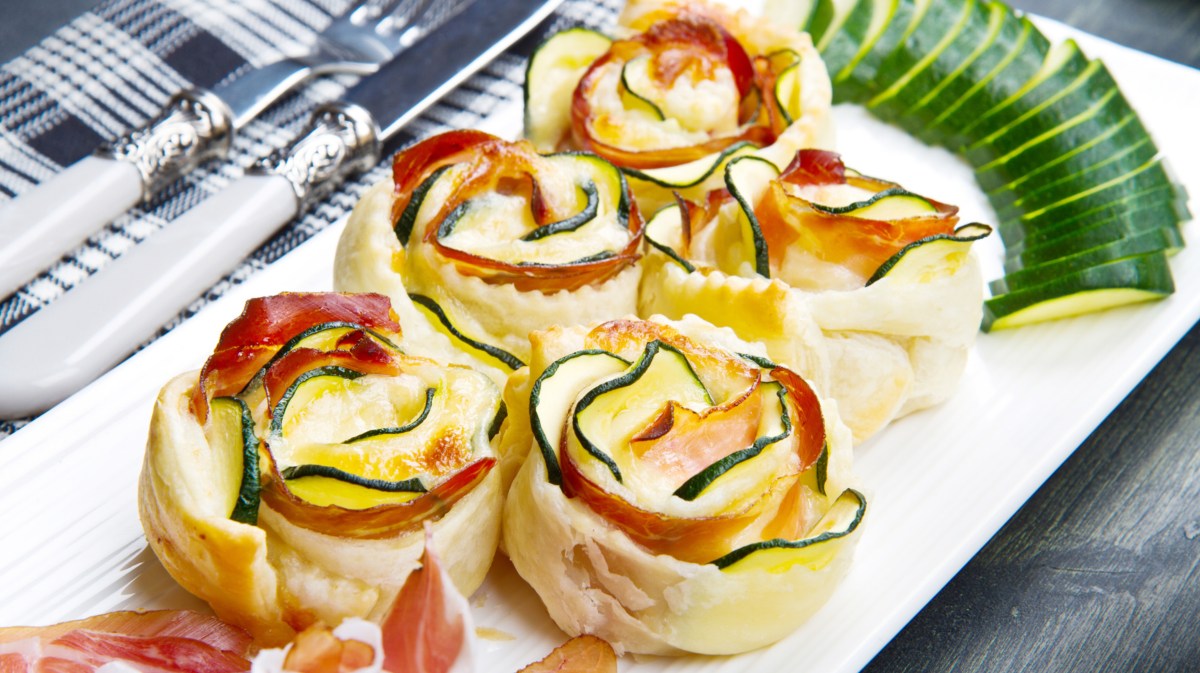 Blätterteig-Rosen gefüllt mit Zucchini, Käse und Schinken auf einem weißen Teller.