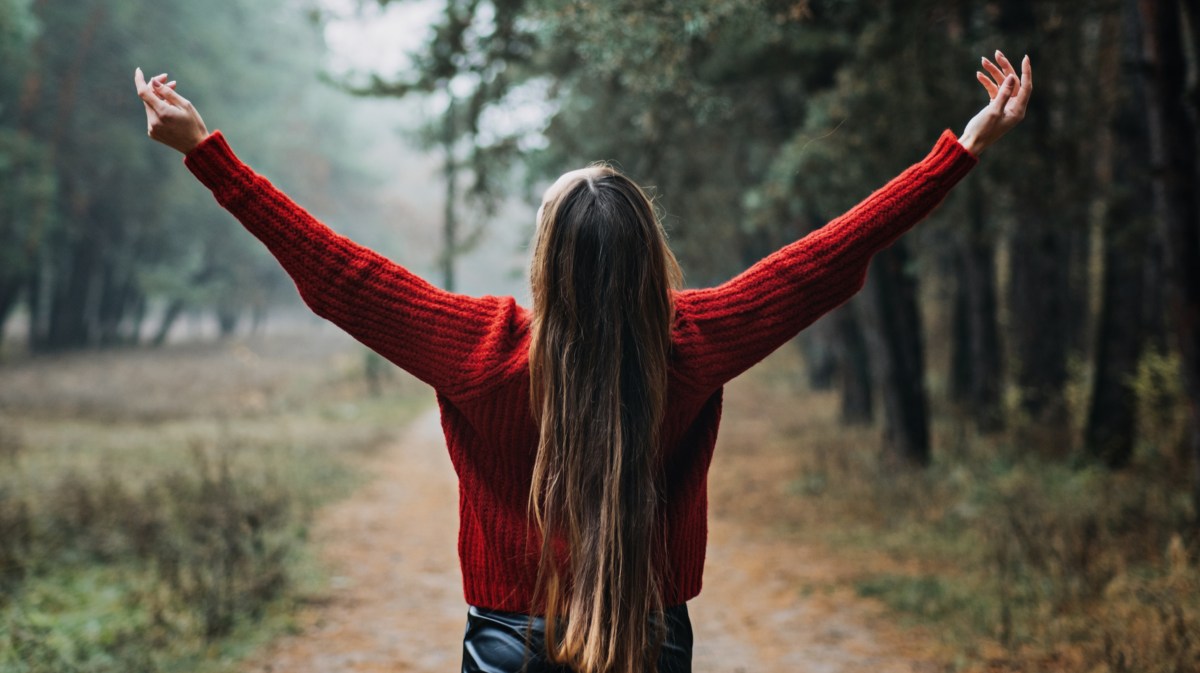 Frau steht im Wald und breitet Arme aus.