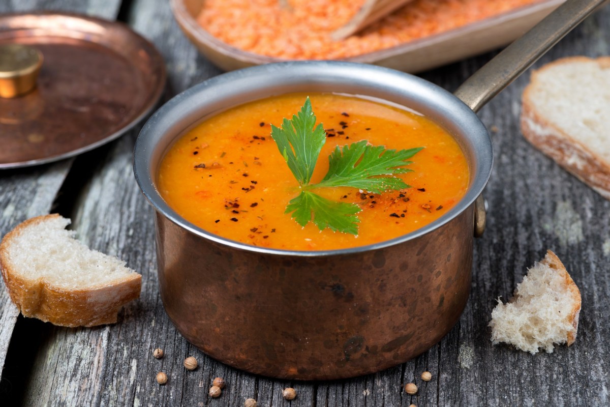 Eine Metallschüssel mit orangefarbener Ofengemüse-Suppe, garniert mit Petersilie, in der Nahaufnahme.