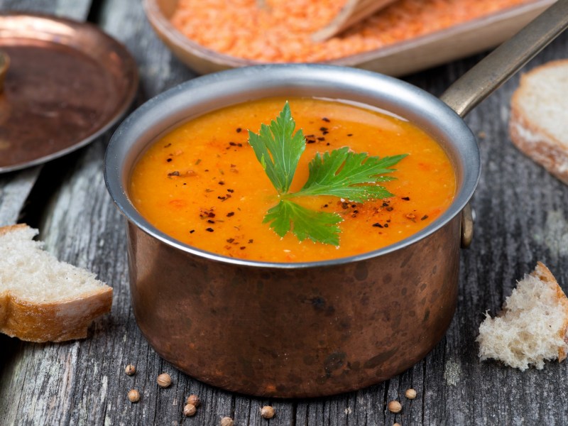 Eine Metallschüssel mit orangefarbener Ofengemüse-Suppe, garniert mit Petersilie, in der Nahaufnahme.
