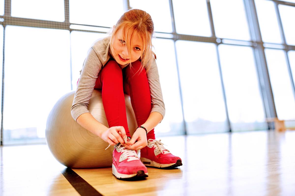 Mädchen sitzt auf einem Gymnastikball und bindet sich die Schuhe.