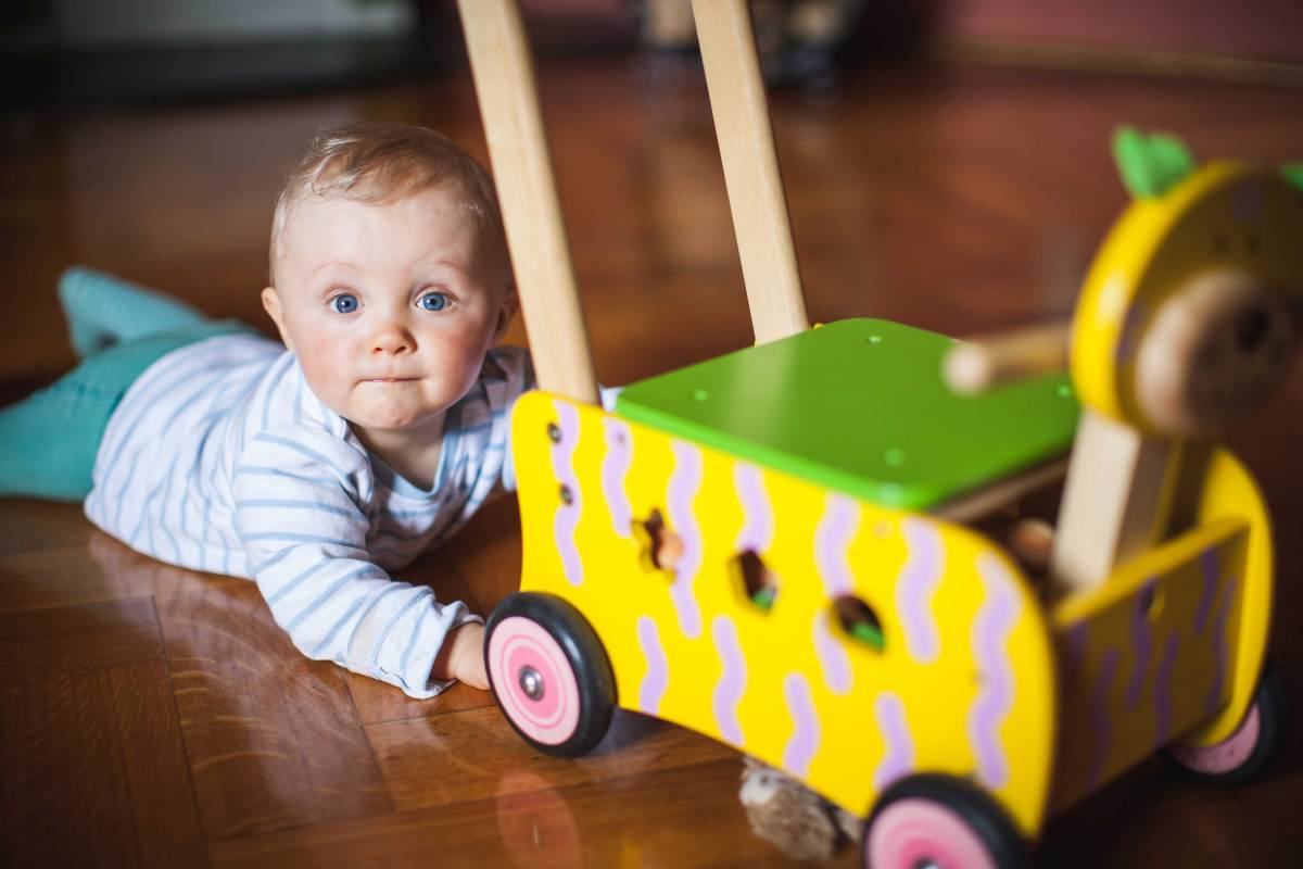 Baby liegt neben einem Lauflernwagen.