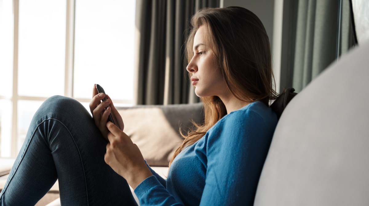 Frau auf dem Sofa, die skeptisch auf ihr Handy schaut