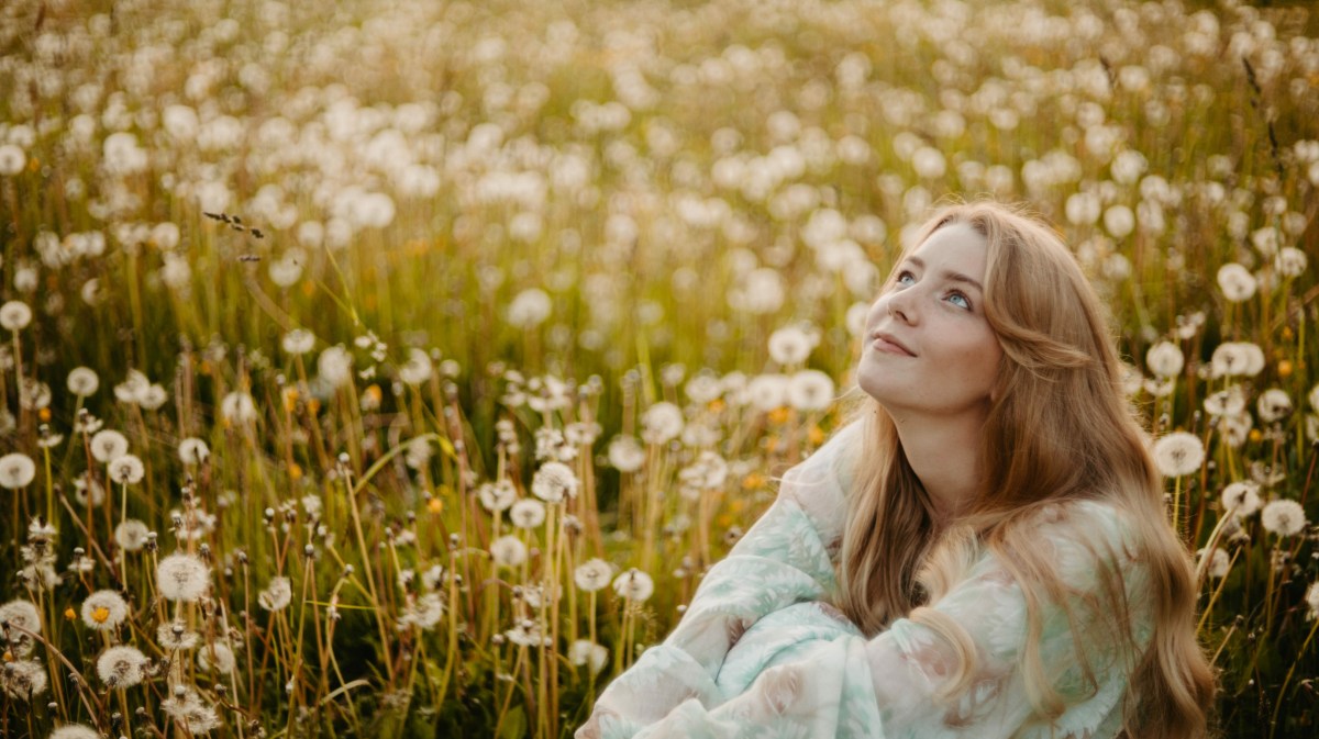 Frau in einem Feld voller Pusteblumen, die in den Himmel schaut und lächelt