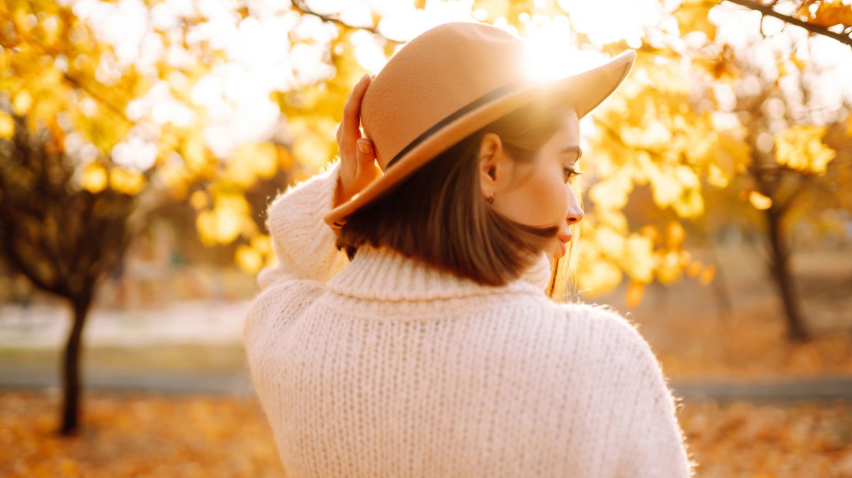 Frau mit Hut und Strickpullover im herbstlichen Wald