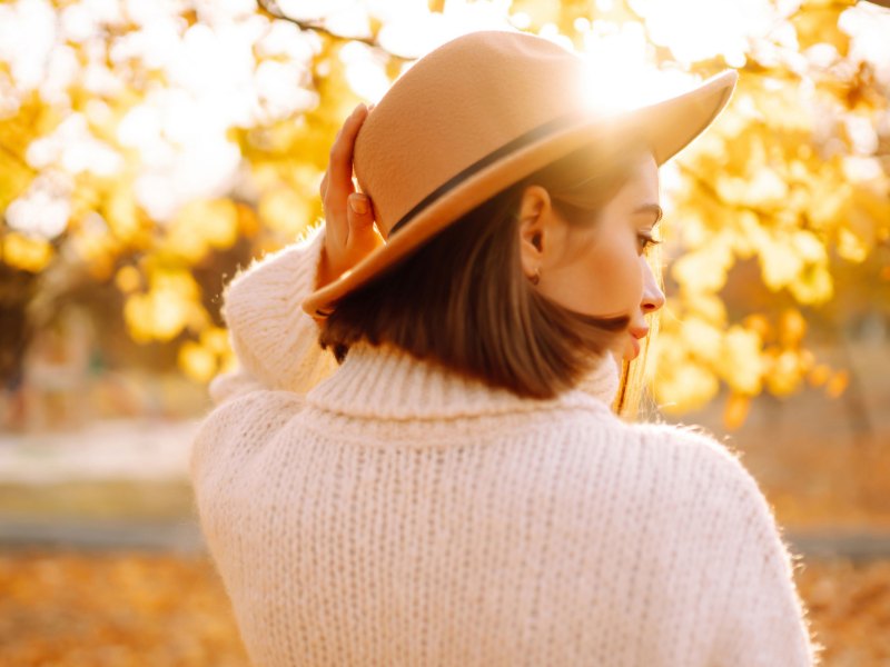Frau mit Hut und Strickpullover im herbstlichen Wald