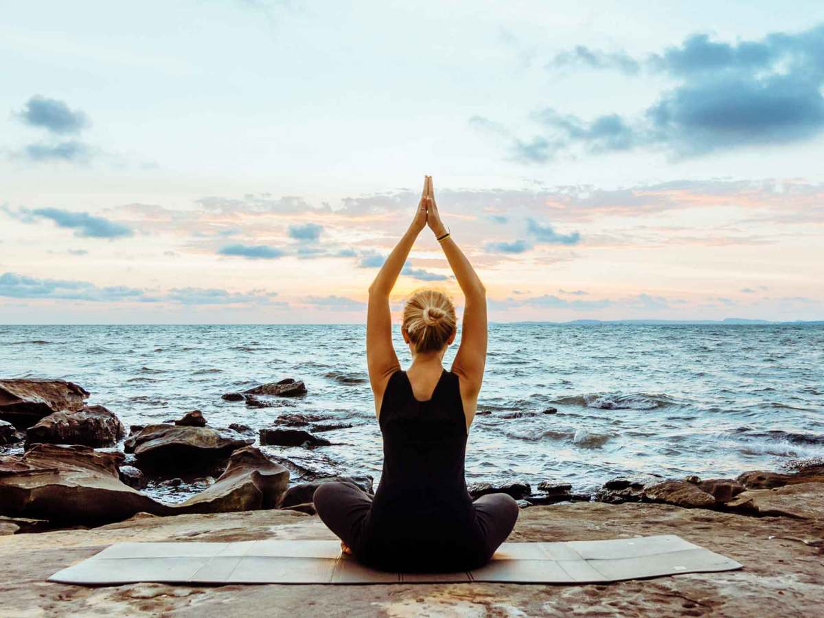 Frau meditiert am Meer vor einer traumhaften Kulisse und dem Sonnenuntergang. .