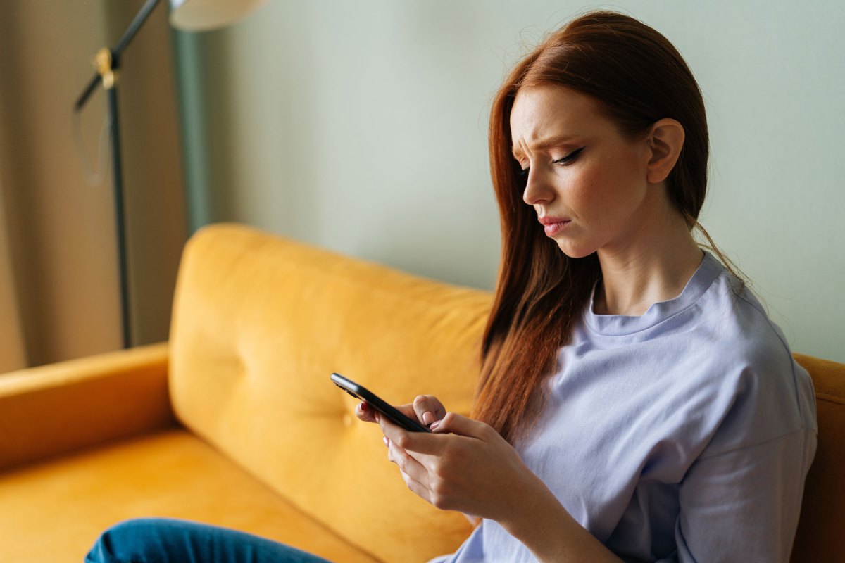 Frau sitzt auf einem gelben Sofa und blickt sorgenvoll