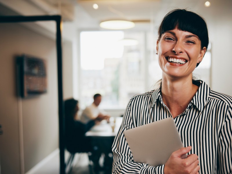 Junge Frau im Job steht im Büro und hält ein Tablet in der Hand.