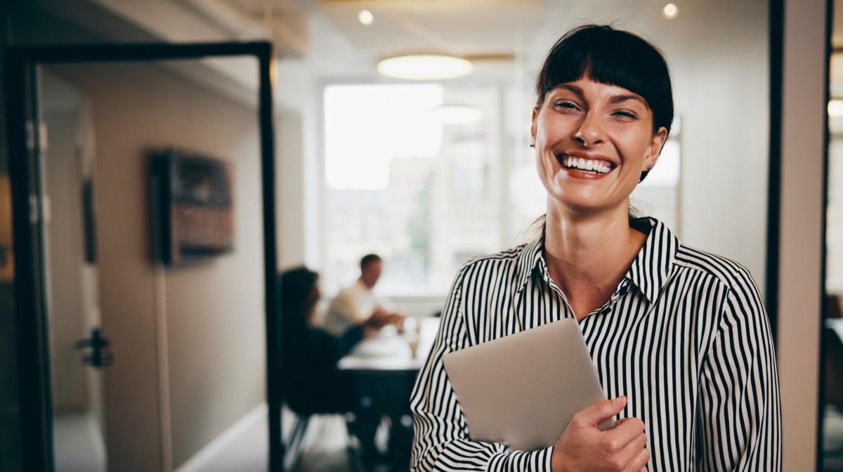 Junge Frau im Job steht im Büro und hält ein Tablet in der Hand.