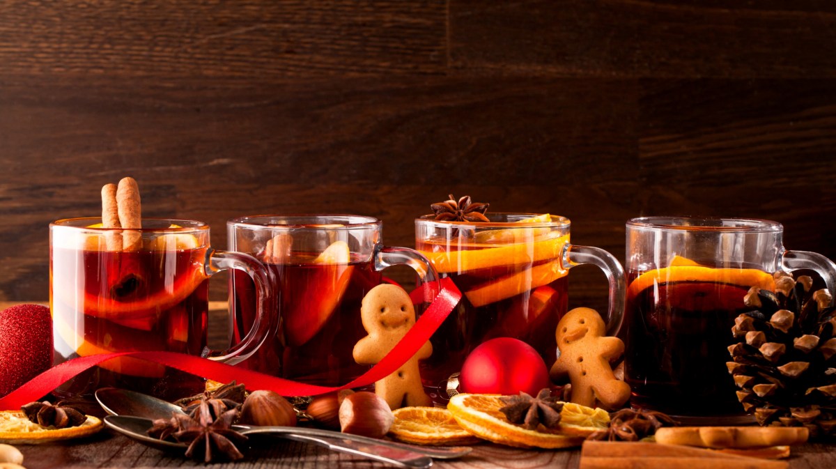 Auf einem weihnachtlich geschmückten Tisch stehen Gläser mit Glühwein, Punsch und Lebkuchenmänner.