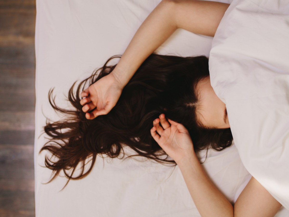 Frau im Bett, die ihre Arme &uuml;ber ihren Kopf streckt