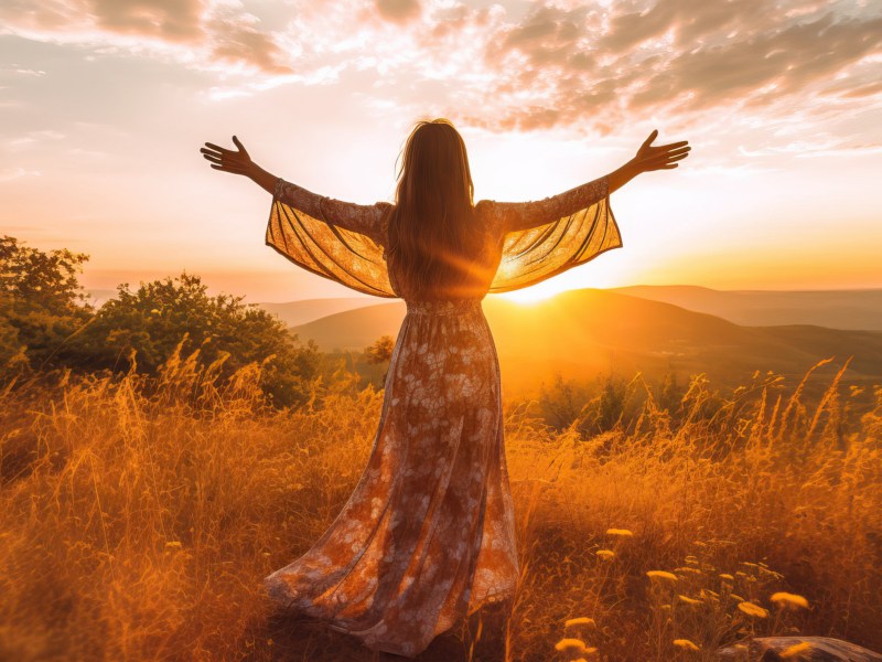 Frau auf einem Feld im Sonnenuntergang in langem Kleid