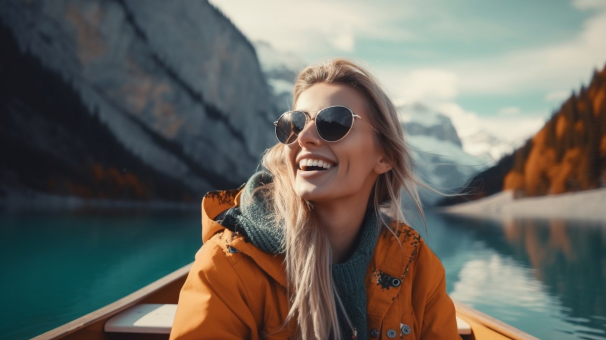 Frau auf einem Boot, die mit Sonnenbrille in die Ferne schaut, während im Hintergrund Berge zu sehen sind