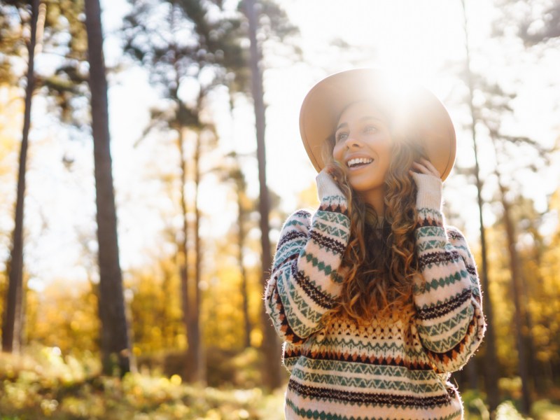 Frau im Wald, die lacht und von der Sonne beleuchtet wird