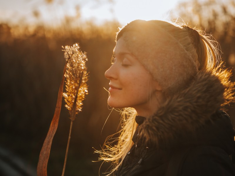 Frau in der Natur, mit Stirnband, die an einem Strauch riecht und die Augen schließt