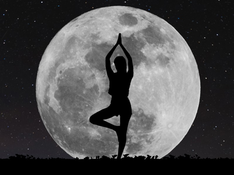 Eine Frau steht vor dem Vollmond und macht Yoga.