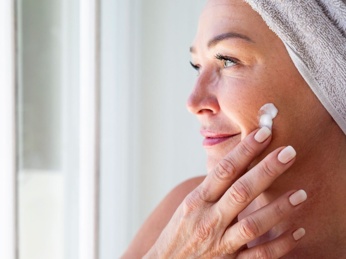 Frau trägt Anti Aging Creme mit Finger auf, sie trägt Turban aus Handtuch