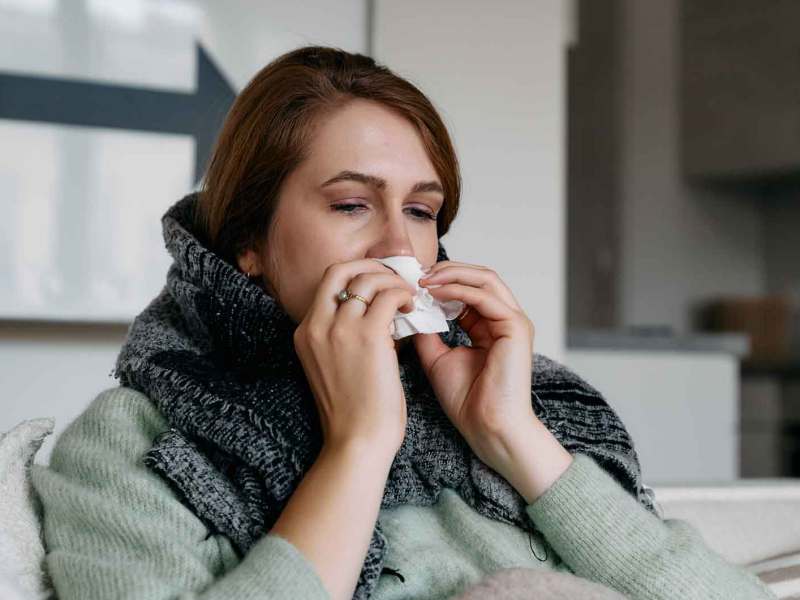 Frau sitzt krank auf der Couch.