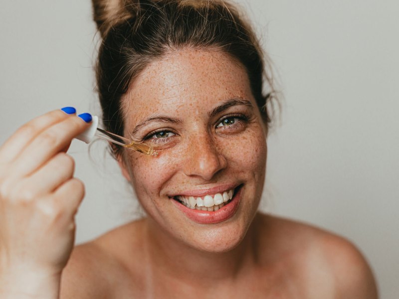 Frau mit Sommersprossen, die sich ein Serum auf die Haut im Gesicht auftr&auml;gt.