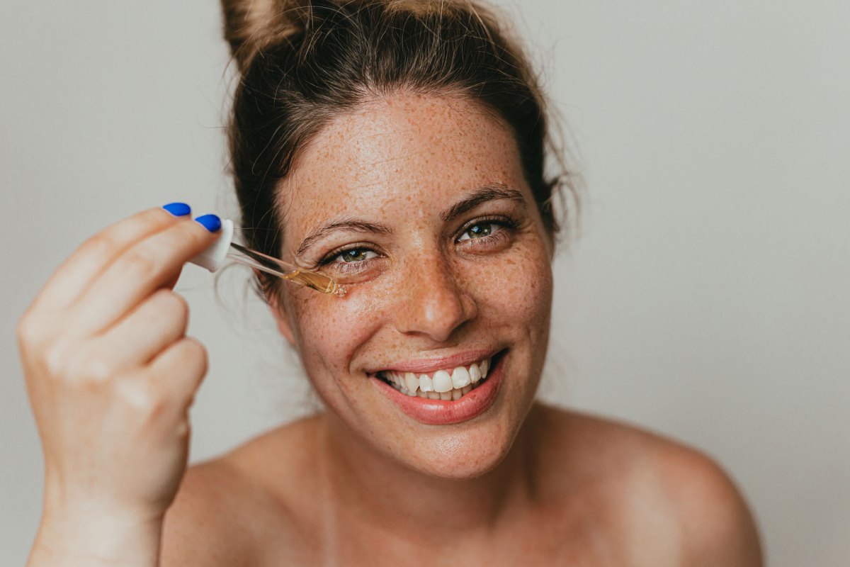 Frau mit Sommersprossen, die sich ein Serum auf die Haut im Gesicht aufträgt.
