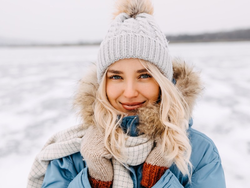 Frau mit blonden Haaren und Mütze im Schnee.