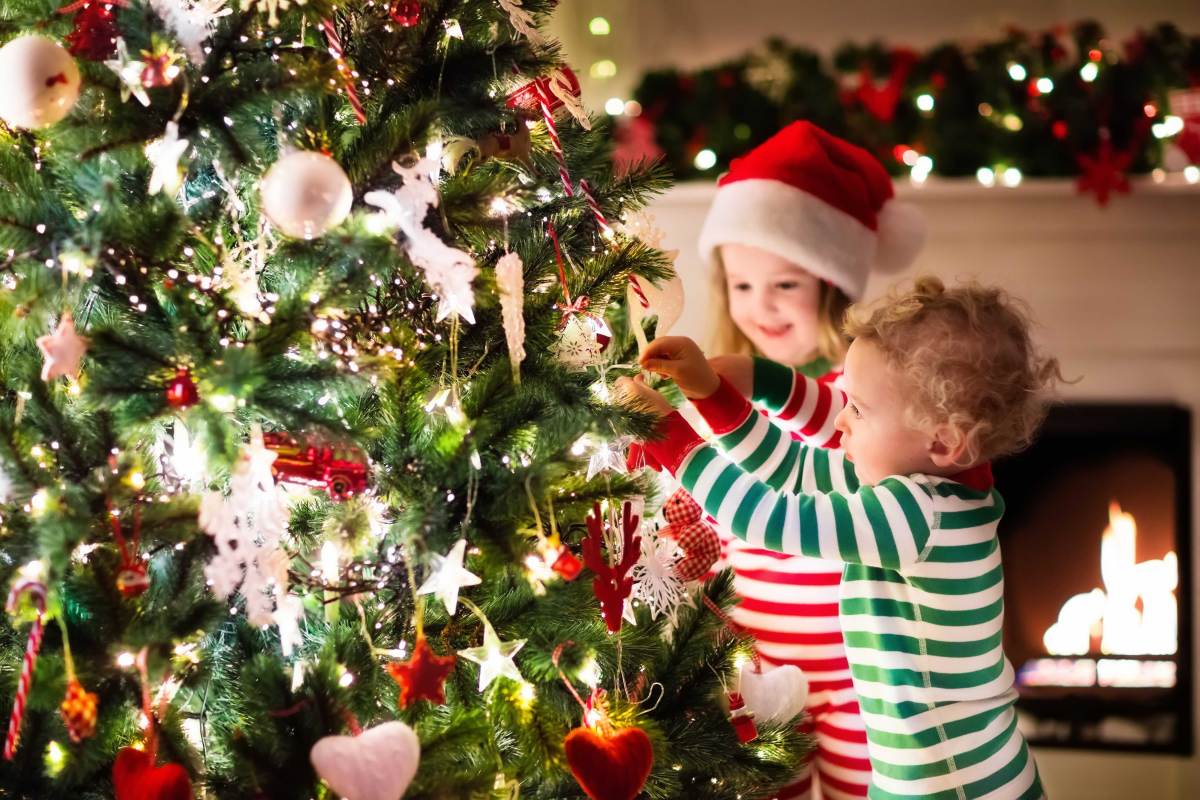 Zwei kleine Kinder schmücken in Schlafanzügen den Weihnachtsbaum.