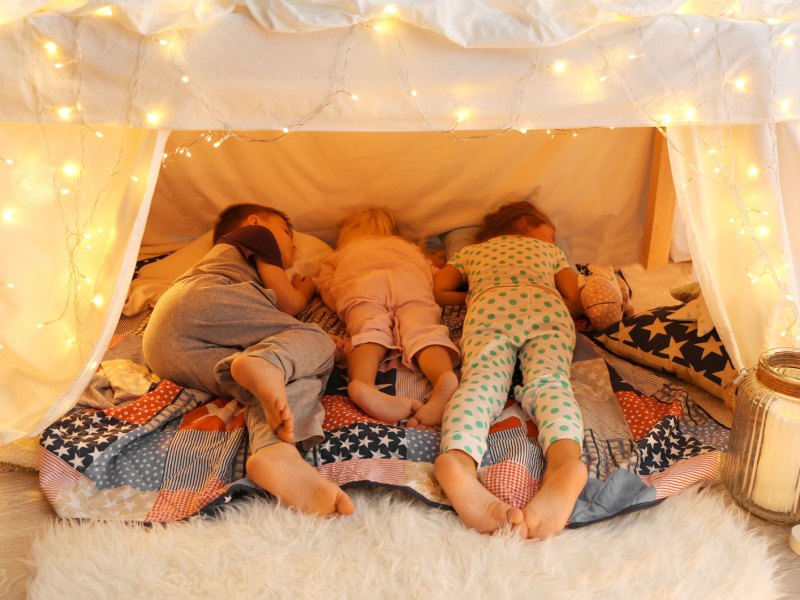Drei Kinder unterschiedlichen Alters schlafen in einer H&ouml;hle im Zimmer.
