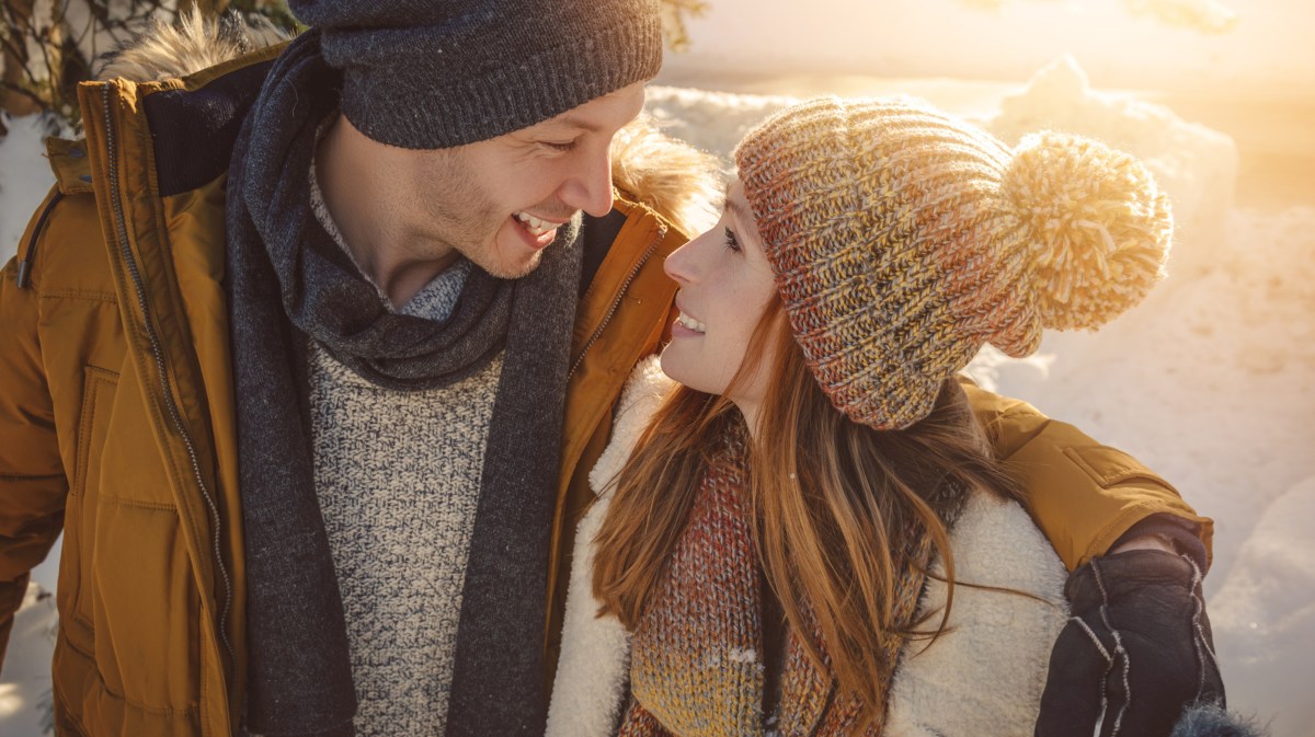 Verliebtes Paar im Schnee mit Winterkleidung schaut sich in die Augen