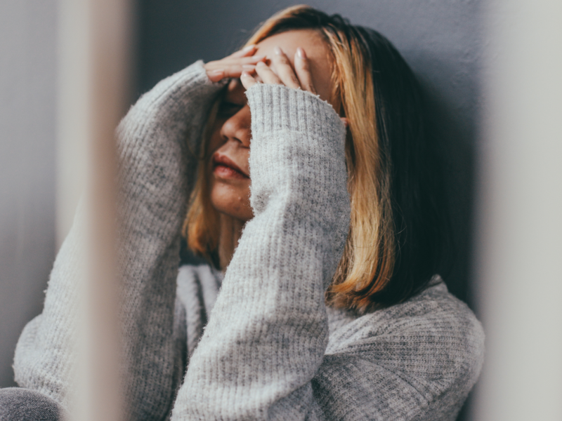 Frau vor einer Wand, die sich die Hände vor dem Gesicht zusammenschlägt