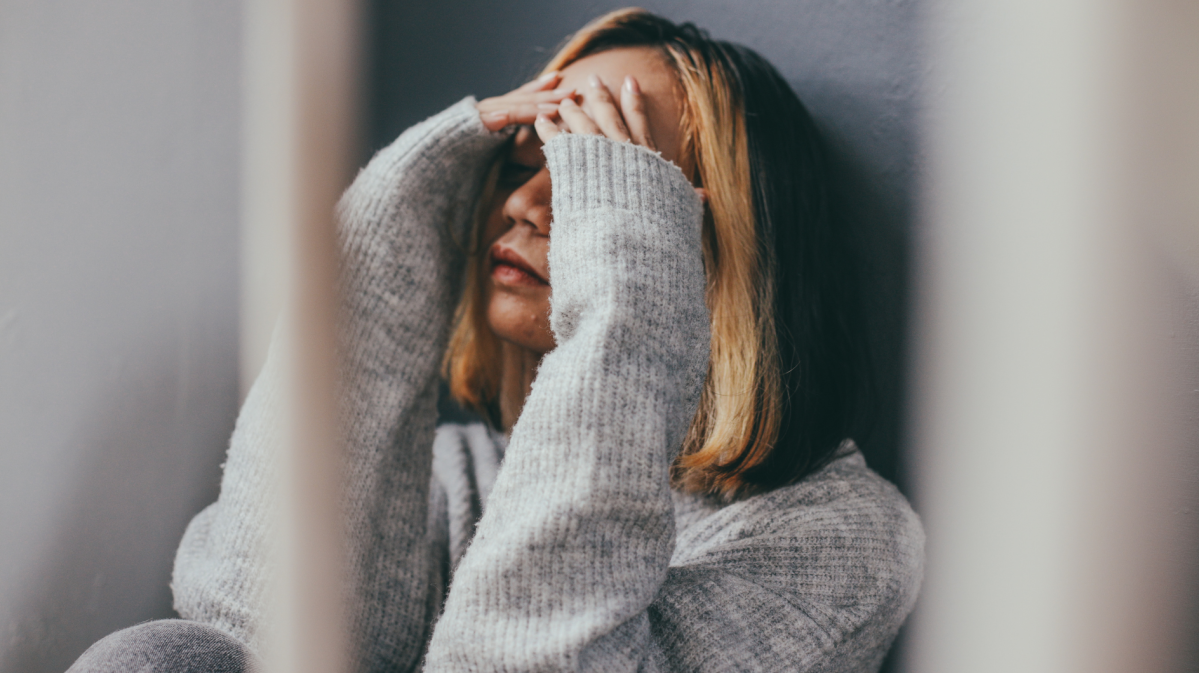 Frau vor einer Wand, die sich die Hände vor dem Gesicht zusammenschlägt