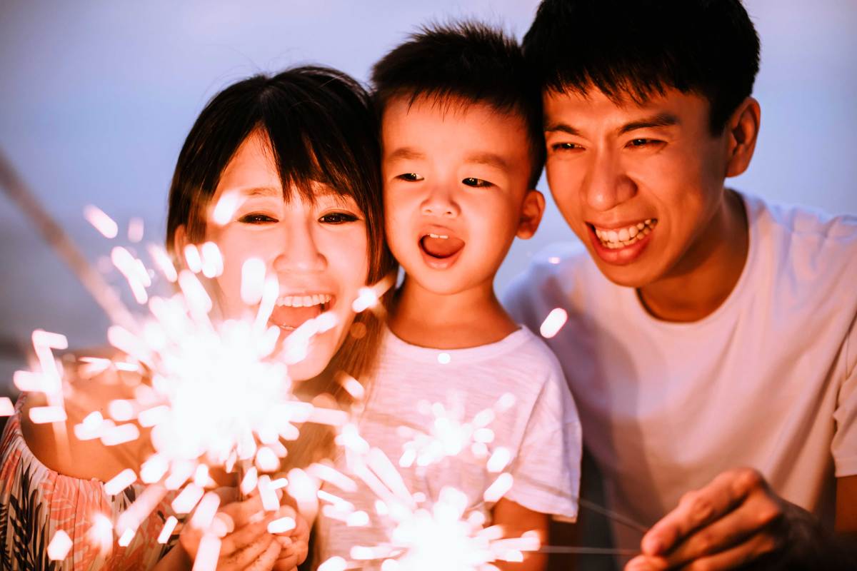 Mutter, Vater und Sohn zünden eine Wunderkerze an.