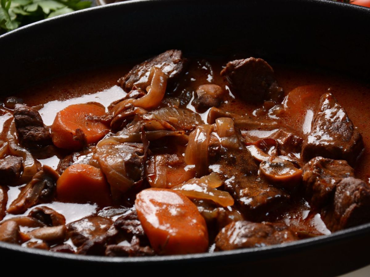 Gulasch mit Karotten und Zwiebeln in schwarzem Topf.