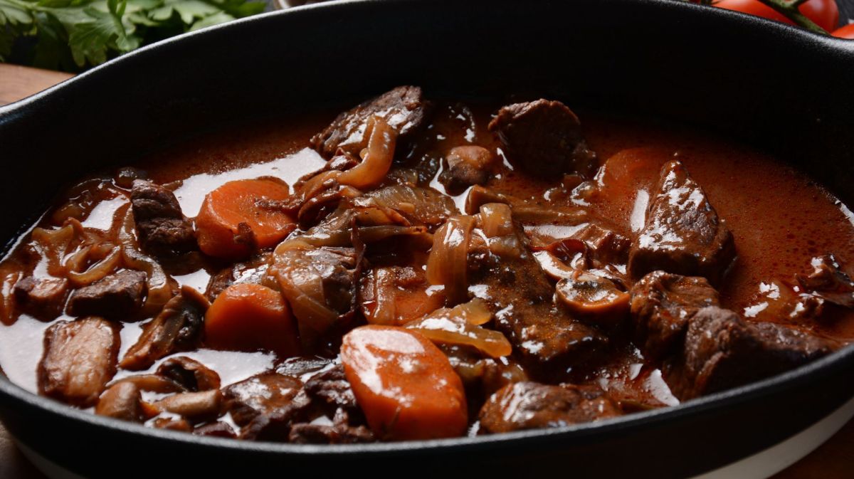 Gulasch mit Karotten und Zwiebeln in schwarzem Topf.