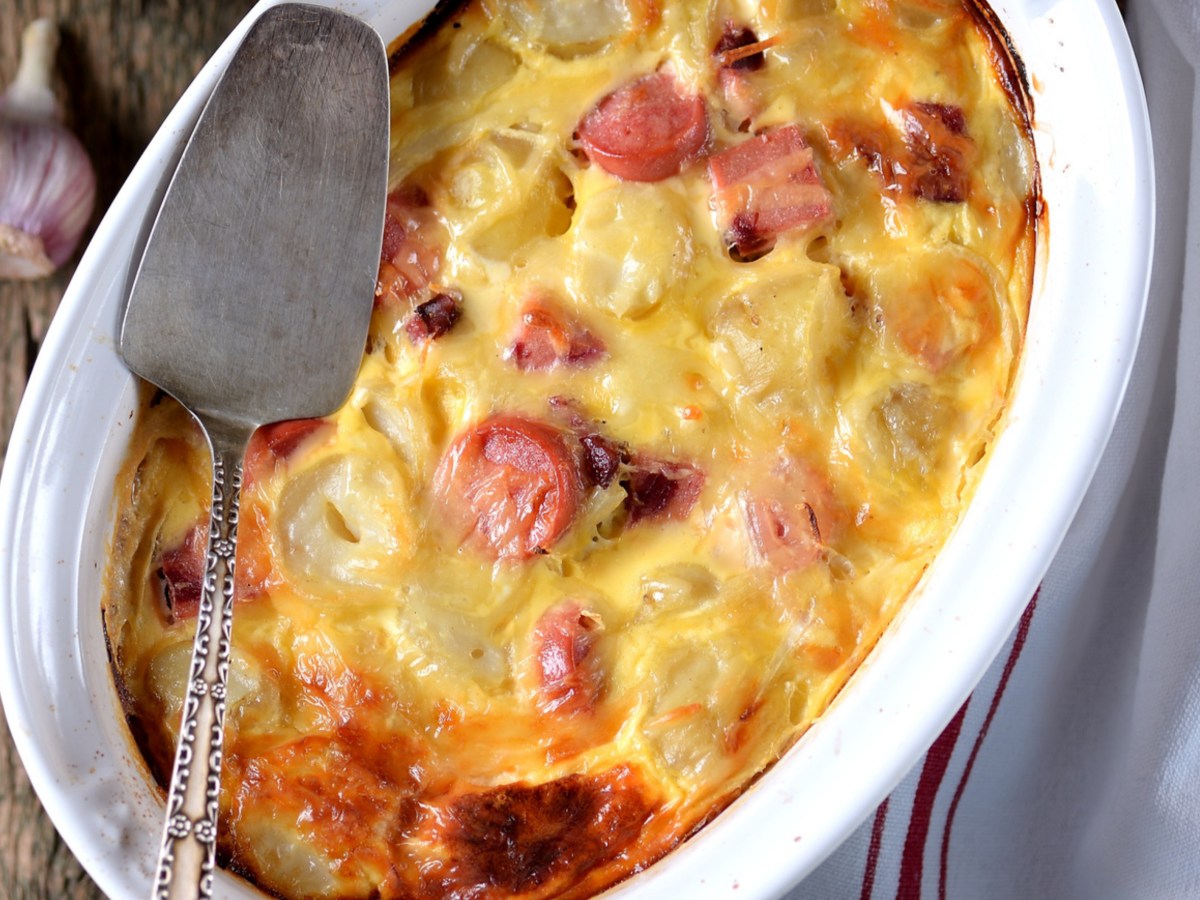 Kartoffelgratin mit Würstchen in weißer Auflaufform.