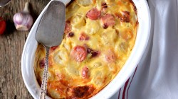 Kartoffelgratin mit W&uuml;rstchen in wei&szlig;er Auflaufform.