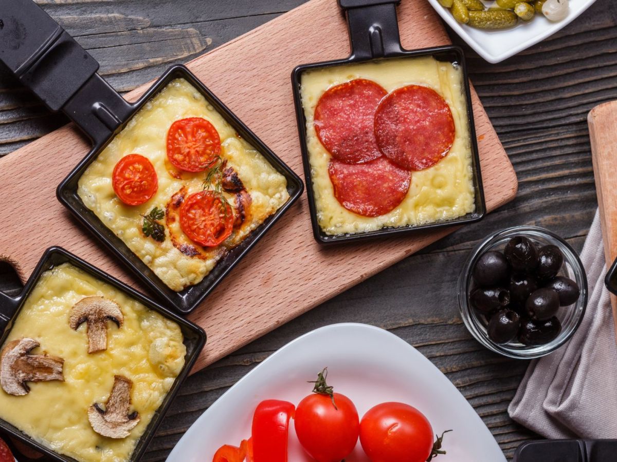 Raclette Pfännchen mit Käse und Zutaten gefüllt.