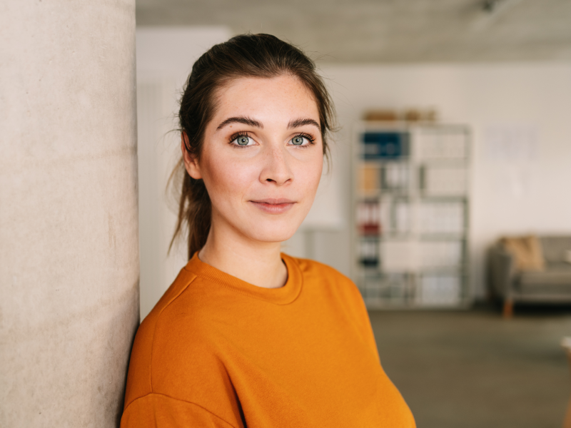 Frau mit orangenem Shirt, die seitlich in die Kamera blickt