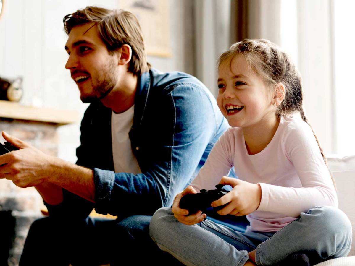 Vater und Tochter sitzen mit Controllern auf dem Sofa und freuen sich.