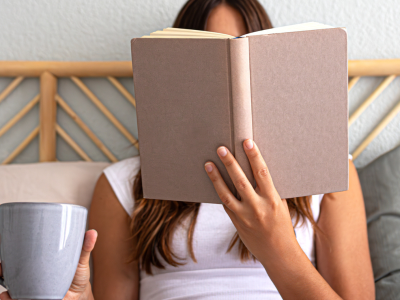 Junge Frau liegt im Bett und liest ein Buch und trinkt einen Tee