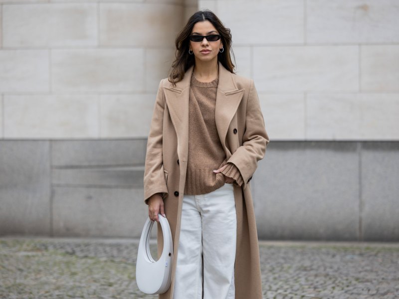 Influencerin, die zur weißen Jeans einen beigen Mantel und Pullover kombiniert